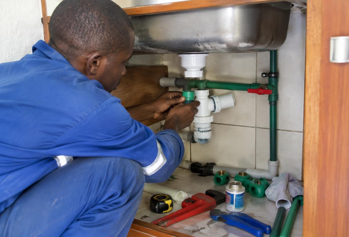 Plumber fitting water pipes and fittings under a kitchen sink